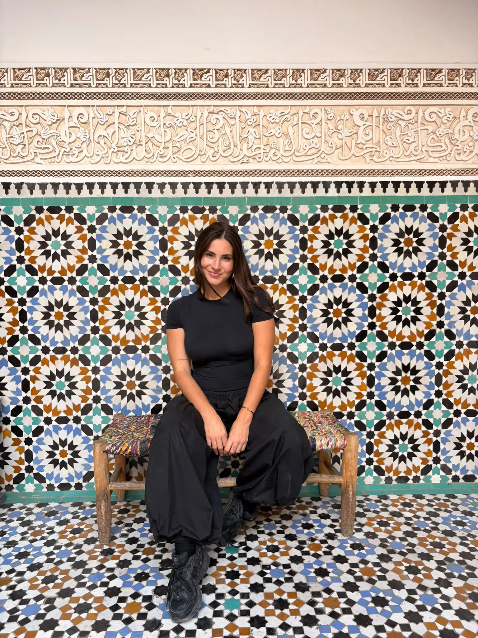 Amalia sentada en un banco de madera frente a una pared de azulejos de colores